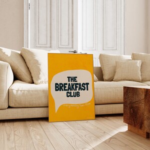May include: A yellow poster with a white speech bubble that says "The Breakfast Club" in black text. The speech bubble also says "every morning 7am-10am" in smaller black text.