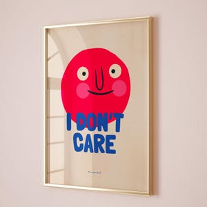 May include: A framed print with a red circle face with a big smile and the text "I DON'T CARE" in blue letters. The print has a light beige background and a gold frame.