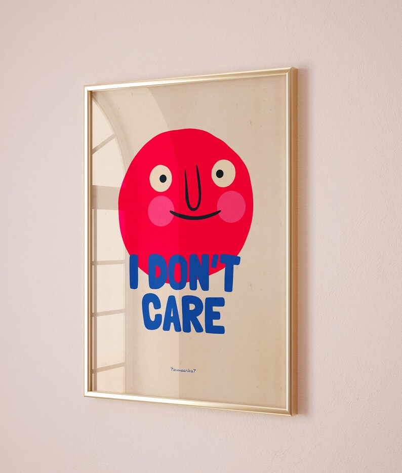 May include: A framed print with a red circle face with a big smile and the text "I DON'T CARE" in blue letters. The print has a light beige background and a gold frame.