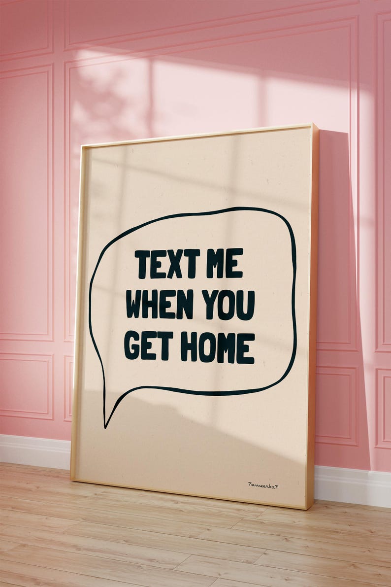 May include: A beige poster with a black speech bubble that says "Text me when you get home". The poster is framed in gold and is hanging on a pink wall.