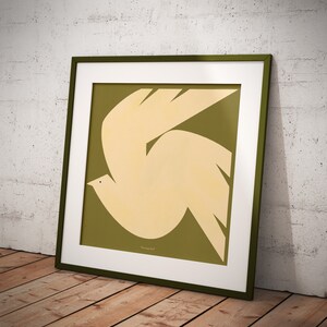 Puede incluir: Una impresi&oacute;n art&iacute;stica enmarcada que presenta una paloma estilizada en crema sobre un fondo verde oliva. La obra de arte est&aacute; enmarcada con un passe-partout blanco y un marco verde oscuro, apoyada contra una pared blanca texturizada y un suelo de madera.