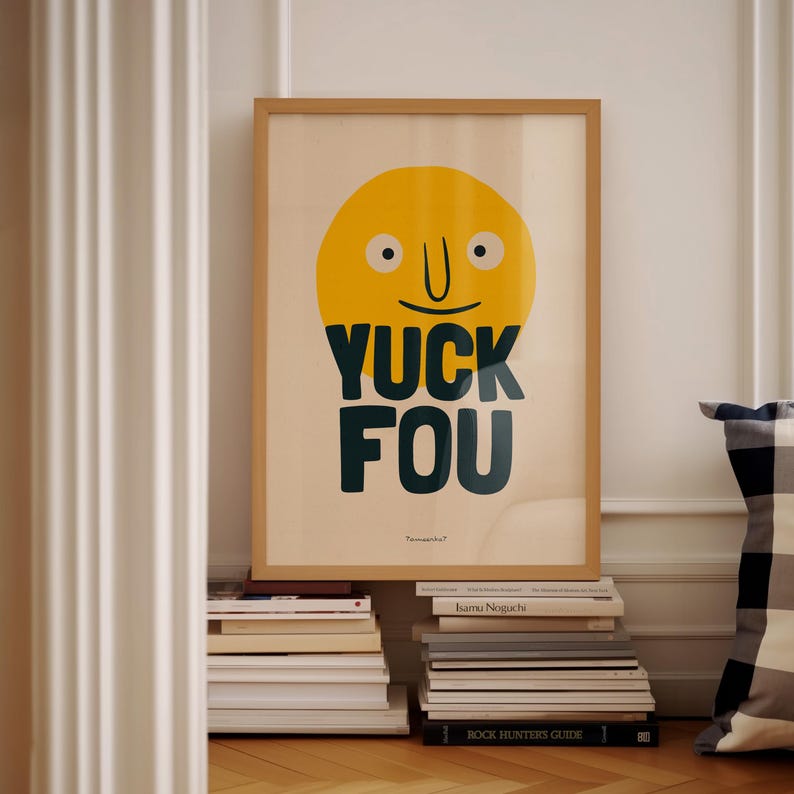 K&ouml;nnte beinhalten: Ein gerahmtes Poster mit einem gelben Smiley-Gesicht und dem Text "YUCK FOU" in dunkelgr&uuml;nen Buchstaben. Das Poster lehnt an einem Stapel B&uuml;cher.