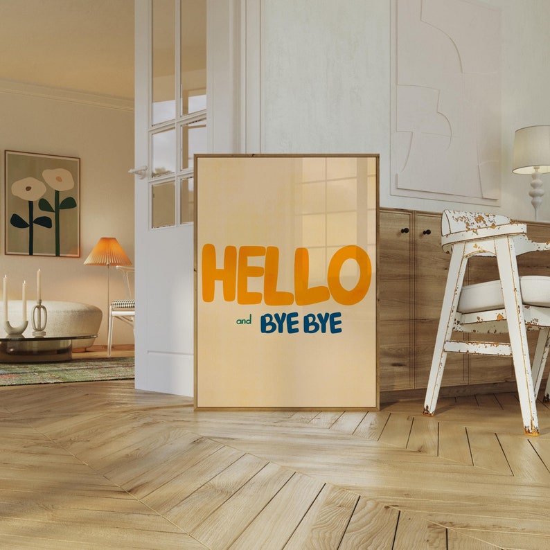May include: A framed print with a light orange background and the text "HELLO and BYE BYE" in a bold, playful font. The text is in yellow and blue.