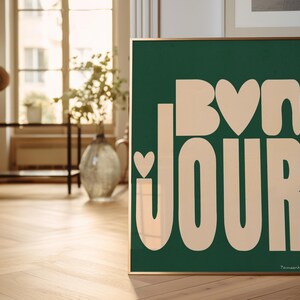 May include: A framed green poster with the text "Bon Jour" in a light peach color. The text is stylized with rounded edges and includes a small heart shape in the "o" of "Bon".