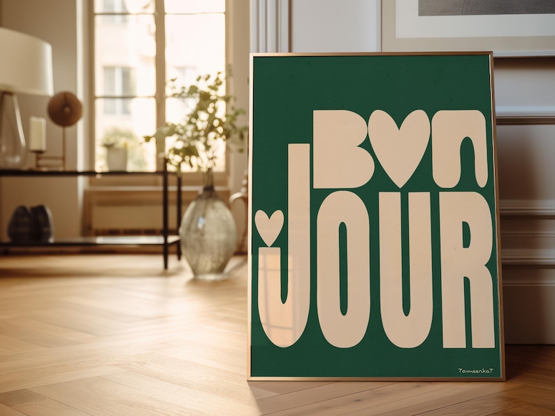 May include: A framed green poster with the text "Bon Jour" in a light peach color. The text is stylized with rounded edges and includes a small heart shape in the "o" of "Bon".