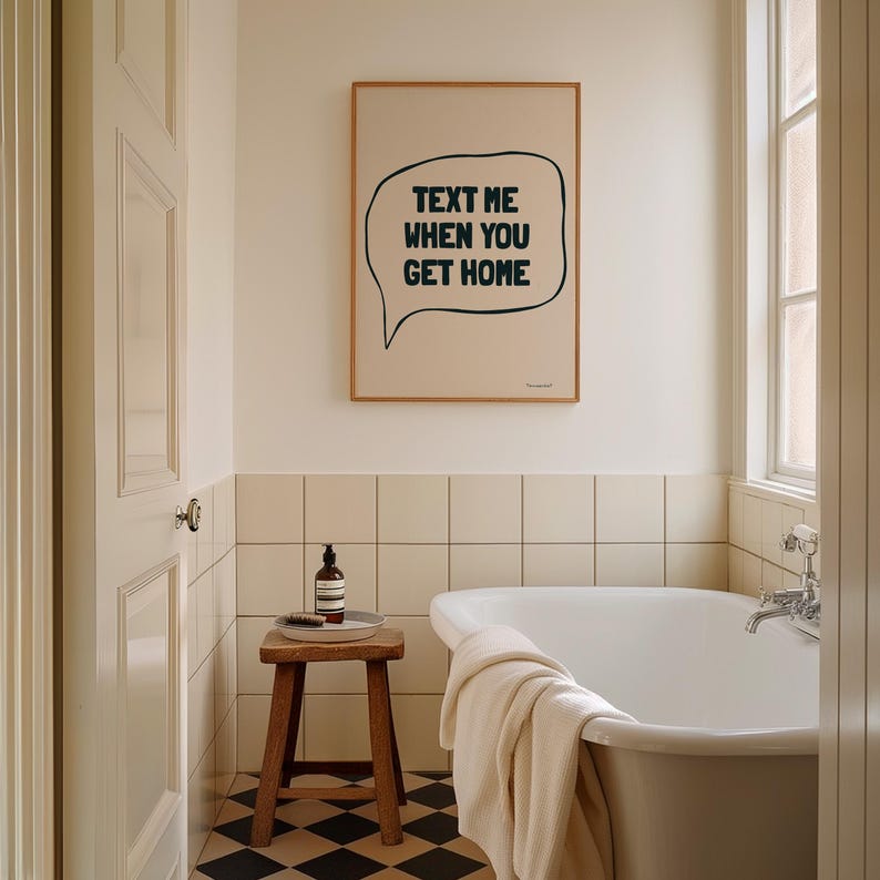 May include: A white bathroom with a bathtub, a wooden stool, and a framed print on the wall. The print features a speech bubble with the text "TEXT ME WHEN YOU GET HOME".