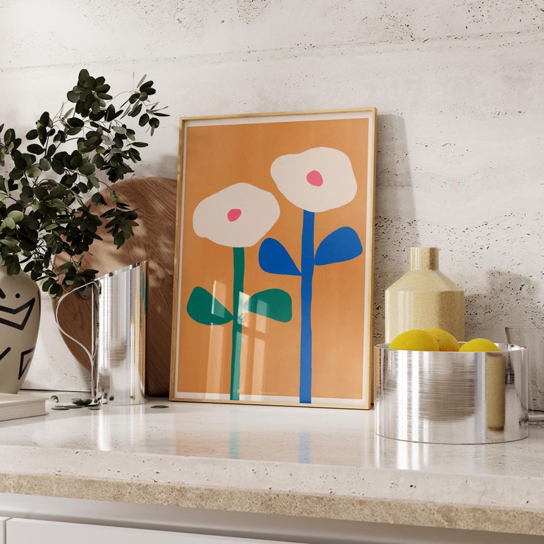 May include: A framed print with a minimalist design featuring two white flowers with pink centers and blue stems on a light orange background.