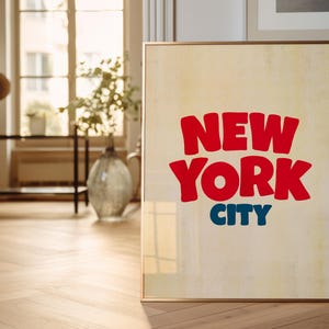 May include: A framed poster with a vintage aesthetic featuring the text "NEW YORK CITY" in bold, red, and blue lettering.
