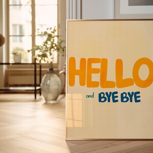 May include: A framed poster with a light yellow background and the words "HELLO and BYE BYE" in large, colorful letters. The word "HELLO" is in orange and the words "BYE BYE" are in blue.