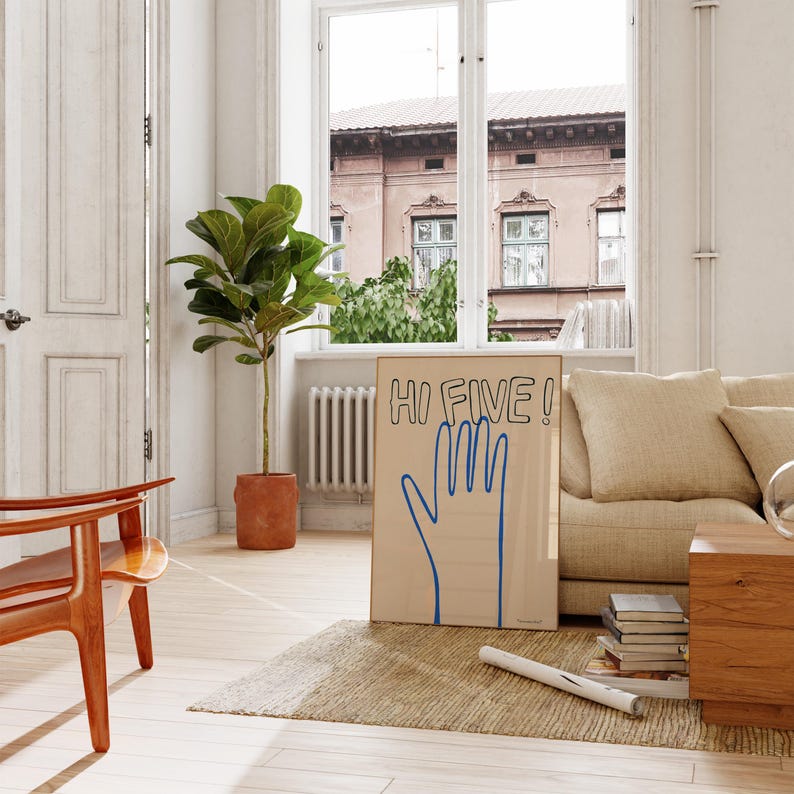 Pu&ograve; includere: Una stampa incorniciata con una mano blu e il testo "HI FIVE!" su uno sfondo beige. La stampa &egrave; appoggiata su un divano beige in un soggiorno.