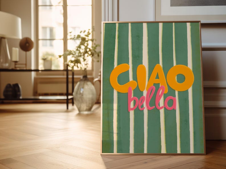May include: A framed art print with a green and white striped background. The words "CIAO bella" are written in orange and pink. The artwork is displayed on a wooden floor in a room with natural light.