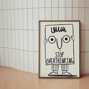 May include: A black and white illustration of a person holding a sign that says "Stop Overthinking". The person has a funny face with big eyes and a small mouth. The sign is in a brown frame.