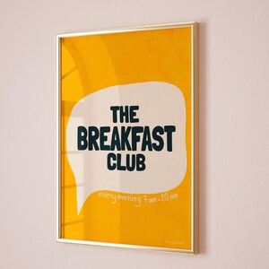May include: A yellow poster with a white speech bubble that says "The Breakfast Club" in black text. The speech bubble also says "every morning 7am-10am" in smaller white text.