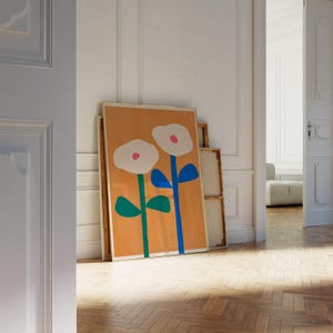 May include: A framed print of two stylized flowers with white petals, pink centers, green stems, and blue leaves on a light orange background.