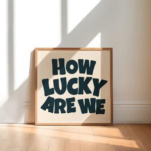 May include: A framed print with a white background and black text that reads "How lucky are we".