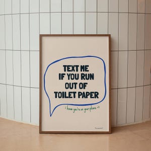 May include: A framed print with a white background and a blue speech bubble that says "TEXT ME IF YOU RUN OUT OF TOILET PAPER". The speech bubble has a green line underneath it that says "i know you're on your phone =>".