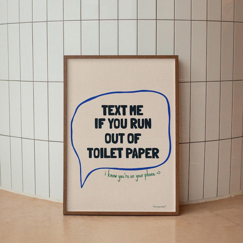 May include: A framed print with a white background and a blue speech bubble that says "TEXT ME IF YOU RUN OUT OF TOILET PAPER". The speech bubble has a green line underneath it that says "i know you're on your phone =>".