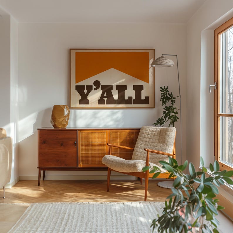 May include: A mid-century modern living room with a wooden cabinet, a white armchair, and a large framed print with the word "Y'ALL" in bold black letters on a yellow and white background.