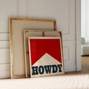 May include: Two wooden framed canvases leaning against a white wall. The smaller canvas has a red and white graphic with the word "HOWDY" in black letters.