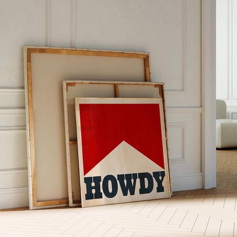 May include: Two wooden framed canvases leaning against a white wall. The smaller canvas has a red and white graphic with the word "HOWDY" in black letters.