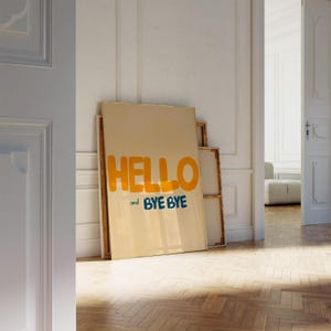 May include: A beige canvas print with the text "HELLO and BYE BYE" in yellow and blue lettering. The print is leaning against a white wall.