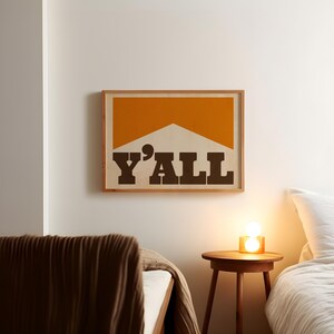 May include: A framed print with a yellow and white geometric design and the text "Y'ALL" in brown letters.
