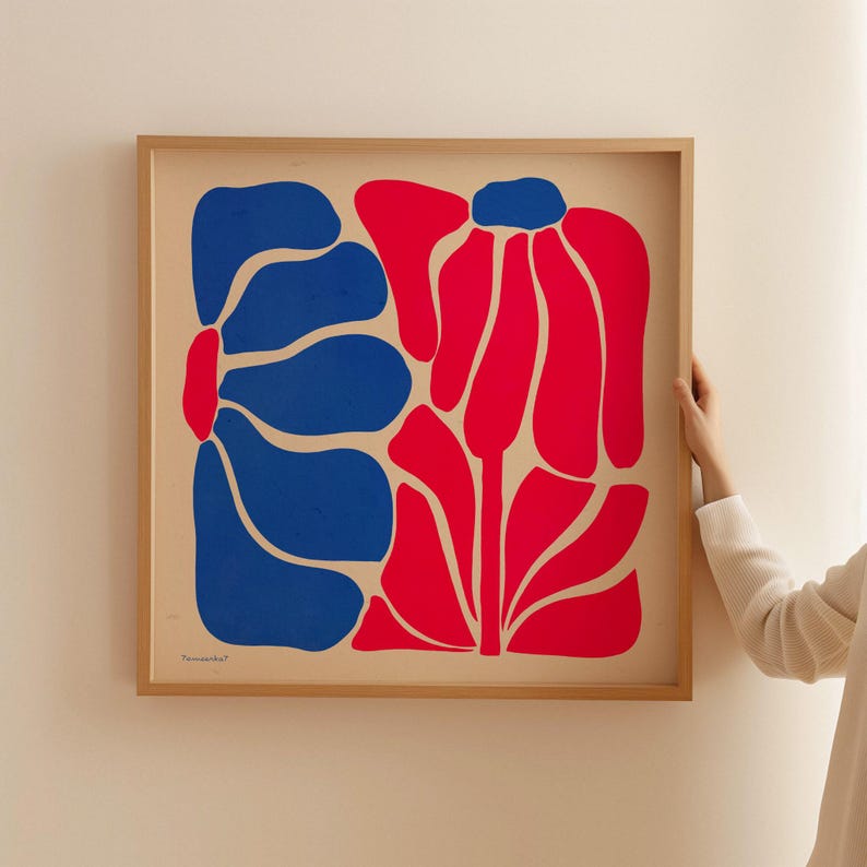 May include: Abstract art print featuring two stylized flowers, one in blue and one in red, on a cream background. The print is framed in a light wood frame.