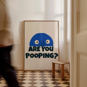 Op de afbeelding: Een ingelijste poster met een blauw cartoonfiguur met twee ogen en een neus. Het figuur kijkt over een witte achtergrond. De tekst op de poster luidt "Are you pooping?"