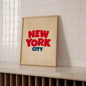 May include: A framed print with a vintage aesthetic featuring the text "NEW YORK CITY" in red and blue lettering on a beige background.