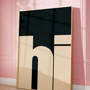 Op de afbeelding: Een ingelijst zwart en beige print met het woord "hi" in vetgedrukte blokletters. De print hangt aan een roze muur.