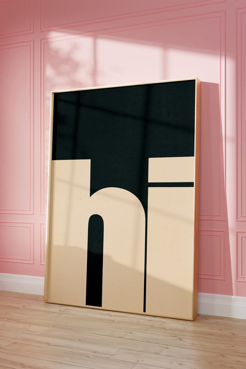 Op de afbeelding: Een ingelijst zwart en beige print met het woord "hi" in vetgedrukte blokletters. De print hangt aan een roze muur.