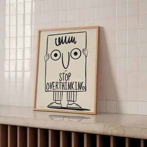 May include: A black and white illustration of a cartoon character holding a sign that says "Stop Overthinking". The character has a big smile and two large eyes.