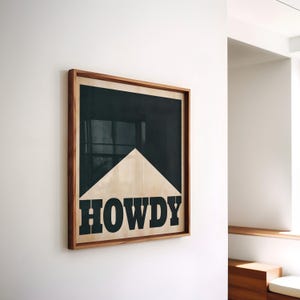 May include: A framed print with a black background and a white triangular shape. The word "HOWDY" is printed in black letters at the bottom of the triangle.