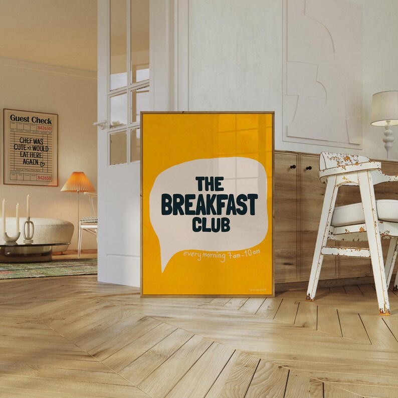May include: A yellow poster with a white speech bubble that says "The Breakfast Club" in black text. The speech bubble has a black outline. The poster has the text "every morning 7am-10am" in black text at the bottom.