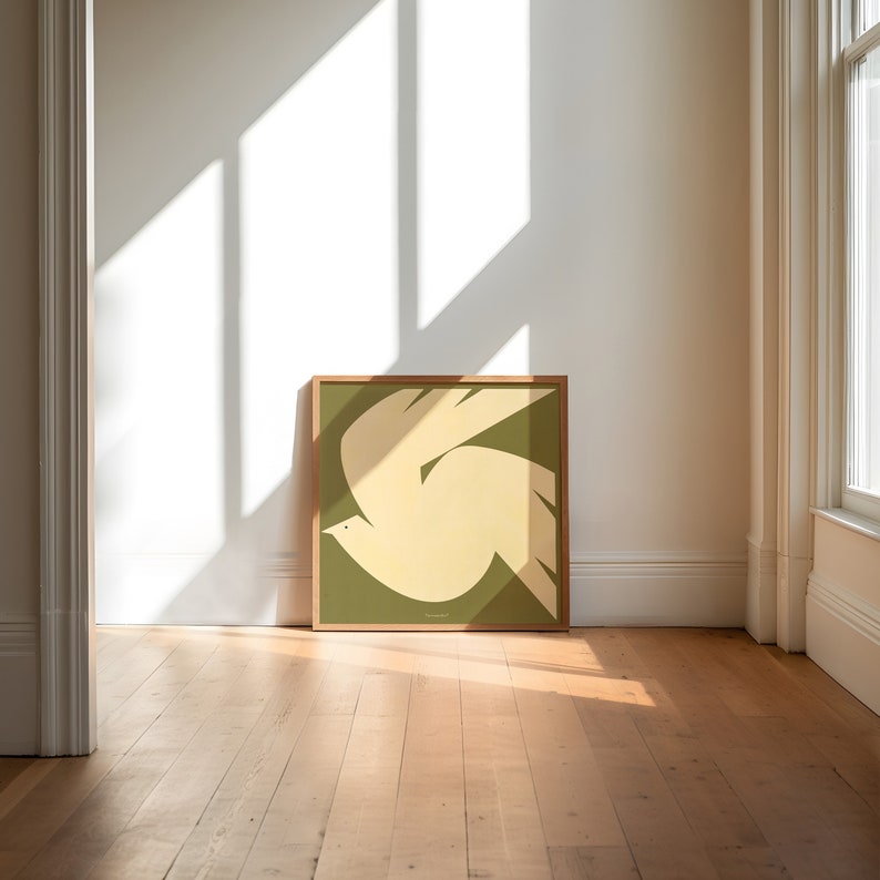 Puede incluir: Un cuadro enmarcado con una paloma estilizada en vuelo. La paloma est&aacute; representada en tonos crema y amarillo claro sobre un fondo verde apagado. La obra de arte est&aacute; enmarcada en un marco de madera natural, a&ntilde;adiendo calidez al dise&ntilde;o.