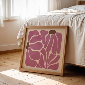 Pu&ograve; includere: Una stampa incorniciata di un design floreale astratto rosa con accenti marroni. La stampa &egrave; in una cornice di legno chiaro e si trova su un pavimento di legno.