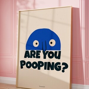 Op de afbeelding: Een ingelijste poster met een blauw cartoonfiguur met twee ogen en een neus. De tekst op de poster luidt "Are you pooping?" met het woord "poop" in grote, vetgedrukte letters.