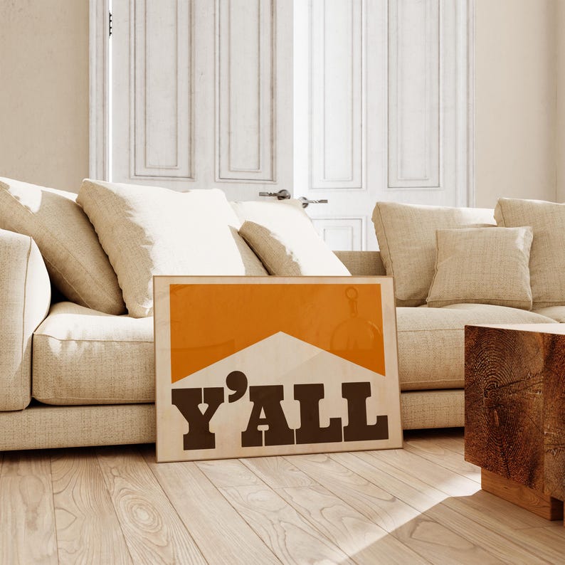 May include: A framed print with an orange background and a white shape resembling a cigarette. The text "Y'ALL" is printed in black letters.