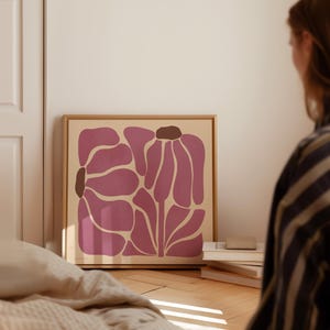 Pu&ograve; includere: Una stampa incorniciata di un design floreale astratto rosa su sfondo crema. Il fiore &egrave; composto da diverse forme sovrapposte.