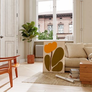 Peut inclure: Une impression d'art abstrait encadr&eacute;e avec une grande fleur orange et des feuilles vertes. L'impression est accroch&eacute;e &agrave; un mur dans un salon avec un canap&eacute;, une chaise et une plante.