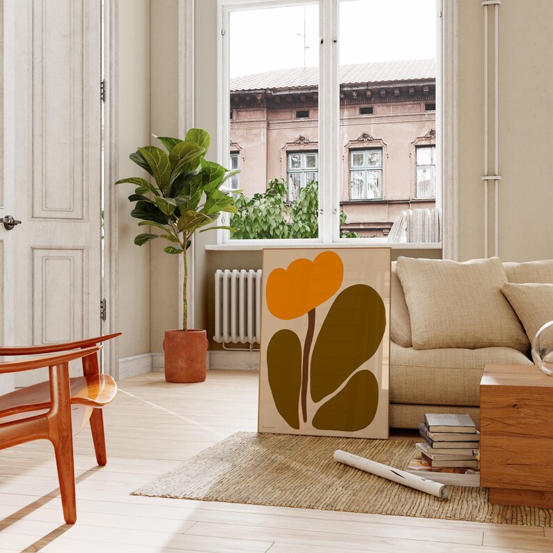 Peut inclure: Une impression d'art abstrait encadr&eacute;e avec une grande fleur orange et des feuilles vertes. L'impression est accroch&eacute;e &agrave; un mur dans un salon avec un canap&eacute;, une chaise et une plante.