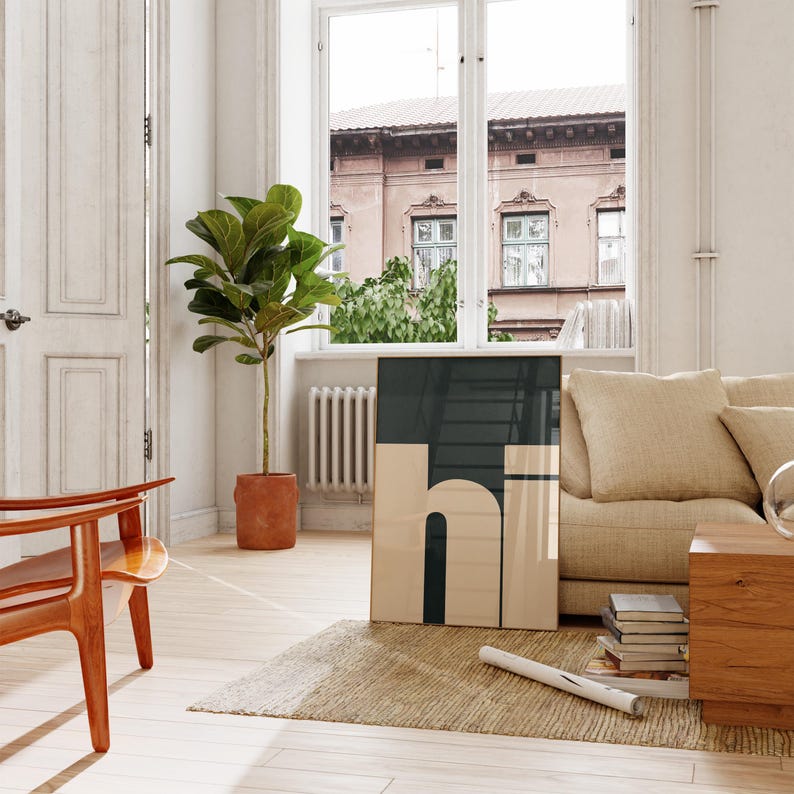 Op de afbeelding: Een beige bank met een groot ingelijst afdruk van het woord "hi" in zwarte en beige letters op een donkergroene achtergrond. De afdruk hangt aan een witte muur in een woonkamer met een groot raam en een plant in een pot.