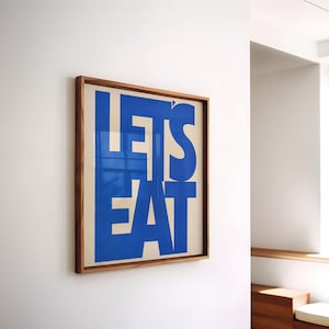 May include: A framed print with the text "LET'S EAT" in bold, blue letters on a white background.