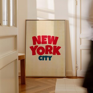 May include: A framed print with a beige background and the text "NEW YORK CITY" in red and blue letters.