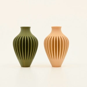 May include: Two ceramic vases with a ribbed design. The vase on the left is green and the vase on the right is peach.