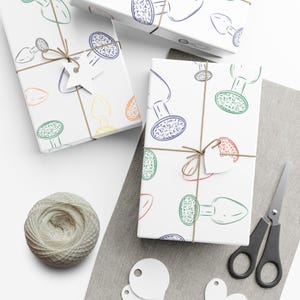 May include: Three wrapped gifts with a white background. The wrapping paper features a repeating pattern of colourful, stylised objects. Each gift is tied with twine and a small tag. A ball of twine, scissors, and blank tags are also visible.