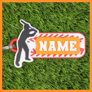May include: A baseball-themed keyring with a white and red design. The keyring features a silhouette of a batter and the word "NAME" in bold white letters on an orange background. The keyring is attached to a red ring.