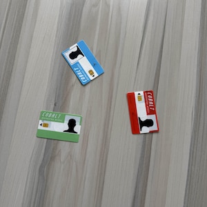 May include: Three rectangular Cobalt access cards in blue, red, and green, each with a silhouette and the text "Cobalt Registered Access". The cards are scattered on a light wood-grain surface.