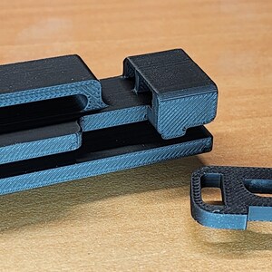 May include: A black plastic 3D printed object with a series of interlocking slots and a separate piece with a hook.