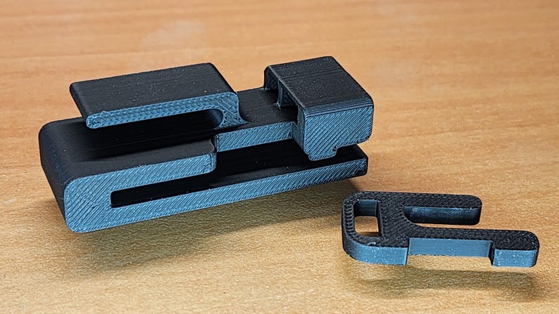 May include: A black plastic 3D printed object with a series of interlocking slots and a separate piece with a hook.